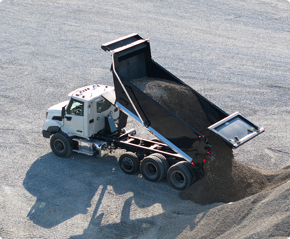 A view from behind of a Volvo VNX that is dumping sand behind it.