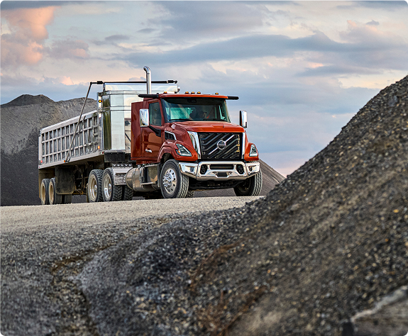A red color Volvo VNX about to climb a rocky uphill area.