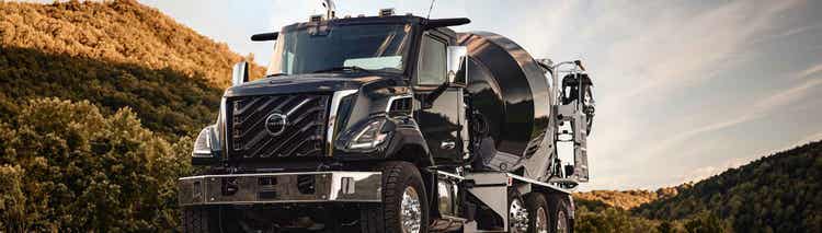 A balck color Volvo VNX truck with a concrete mixer at the back of the truck with hills in the background.