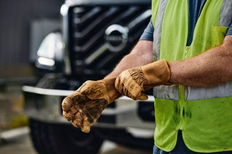 A closeup view of a construction worker fixing his gloves with the Volvo VNX in the background.