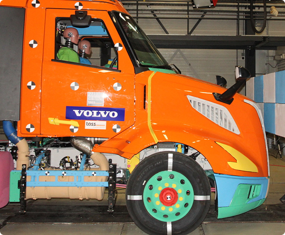 A side view of an orange color Vovlo VNX that has mannequins in the driver and passenger seat.
