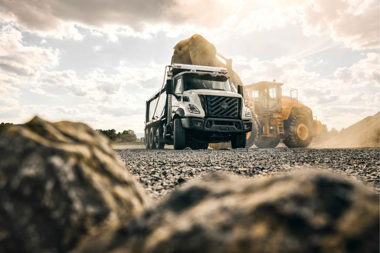 A view from below of the Volvo VNX on a rocky road with a construction vehicle behind it.