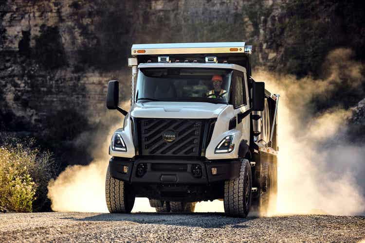 A front view of the Volvo VNX with a driver that's visible driving on a rocky background with smoke on the background.