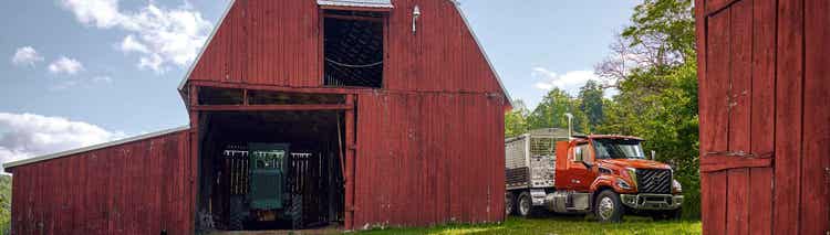 A red Volvo VNX on a farm with a barn beside the truck.
